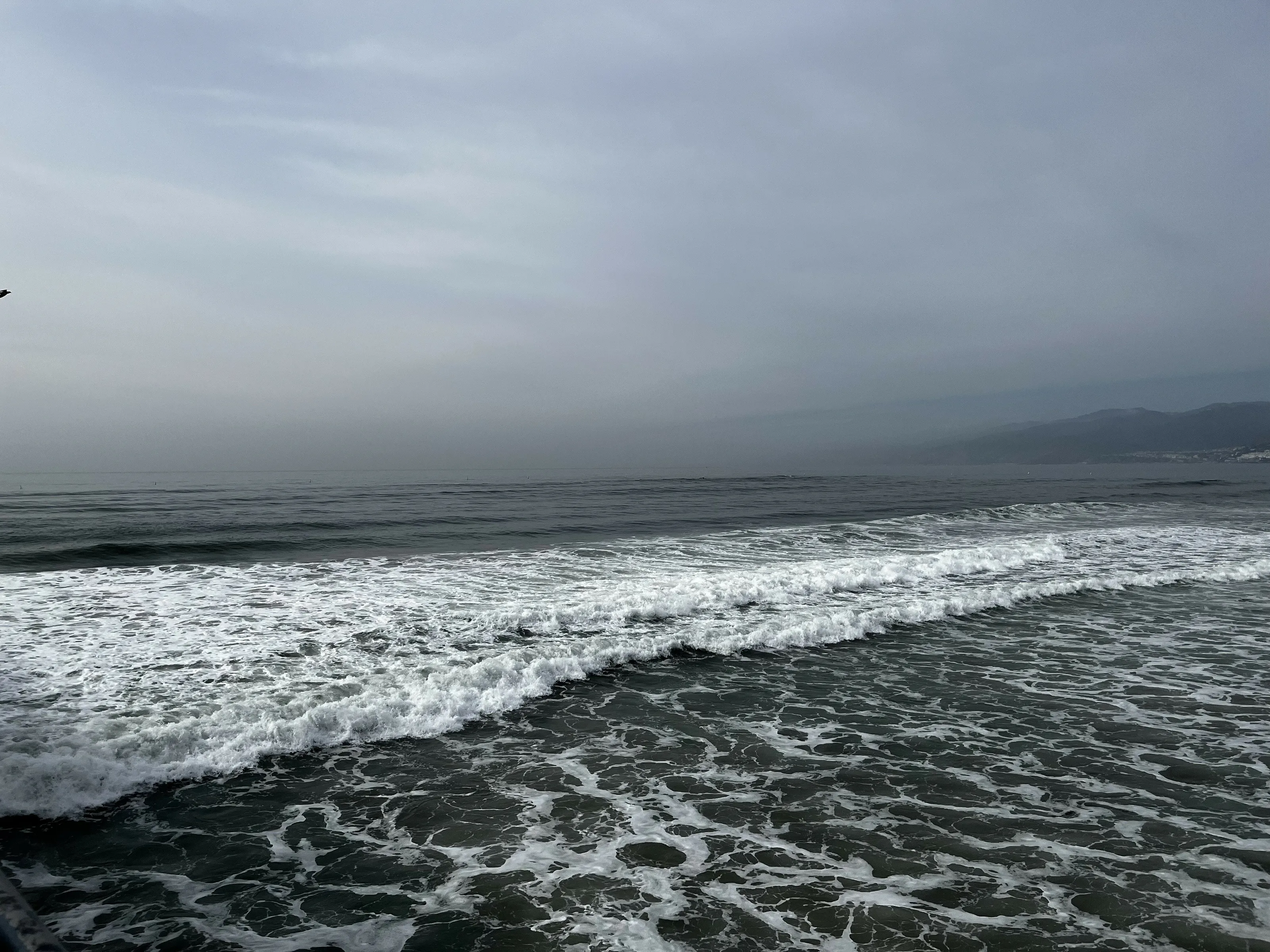 Waves crashing on a foggy beach during early morning light with mountains in the background in Calif