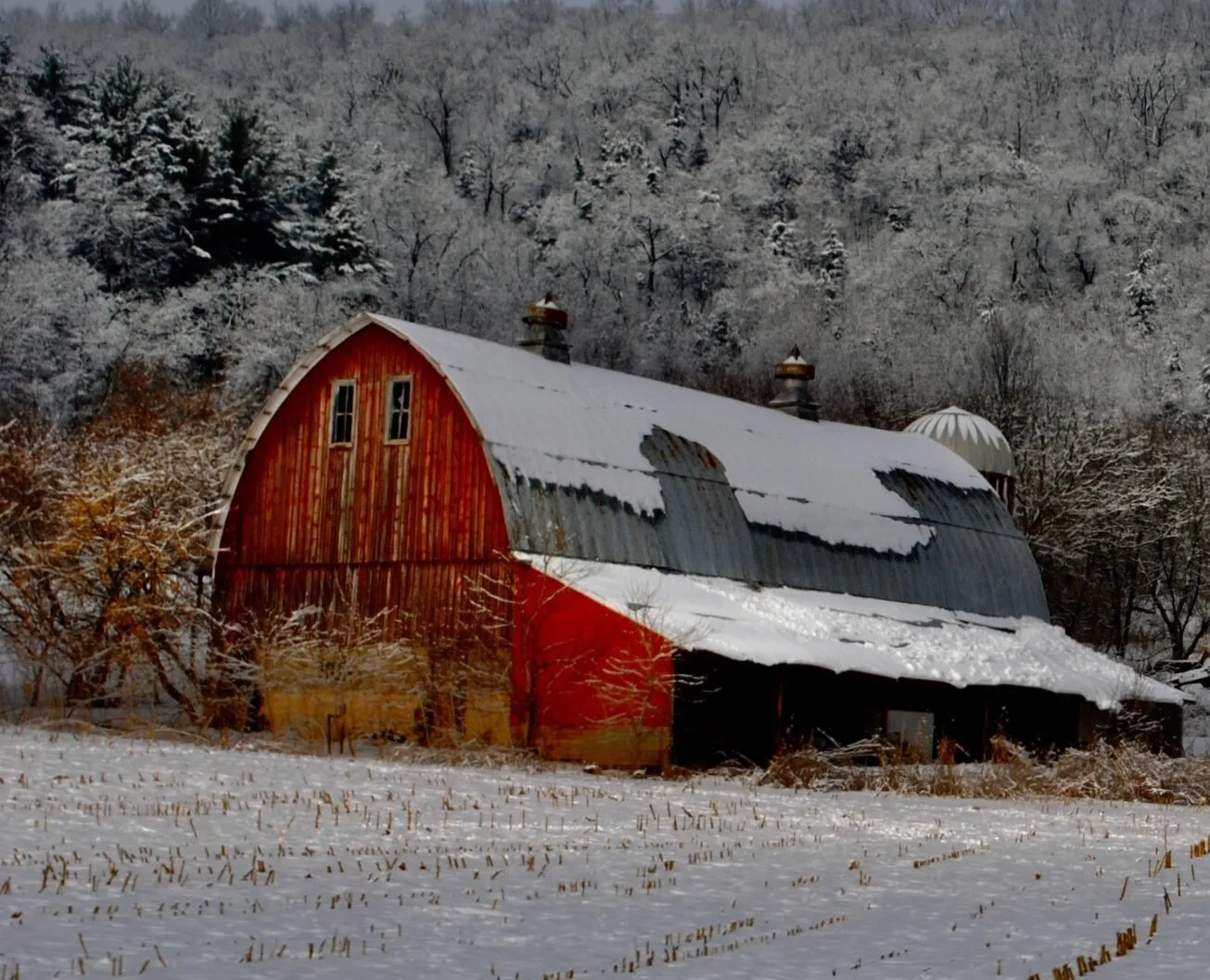 And old farmers barn silhouette against the hillside covered in snow