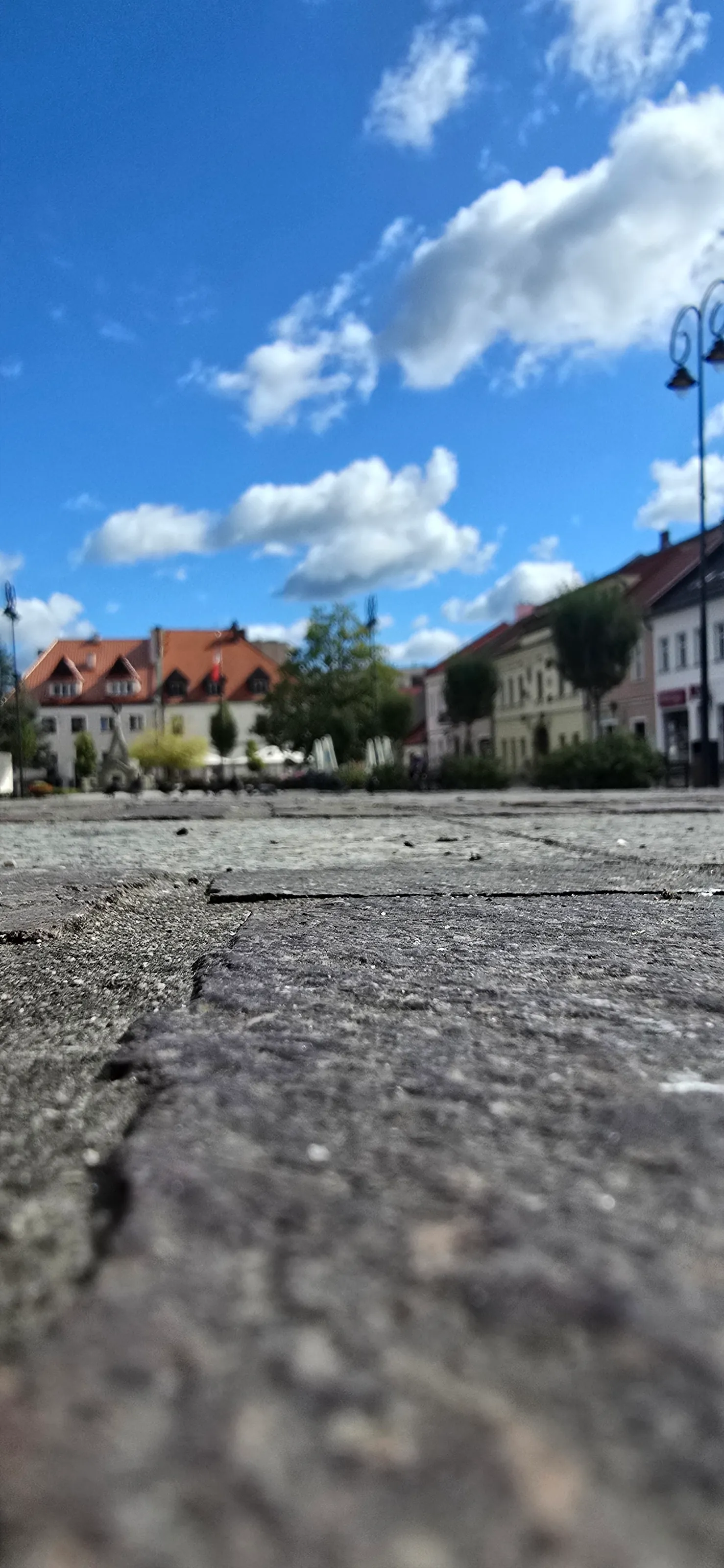 „The market square in Myślenice bustling on a sunny day, with historic buildings, local shops, and c