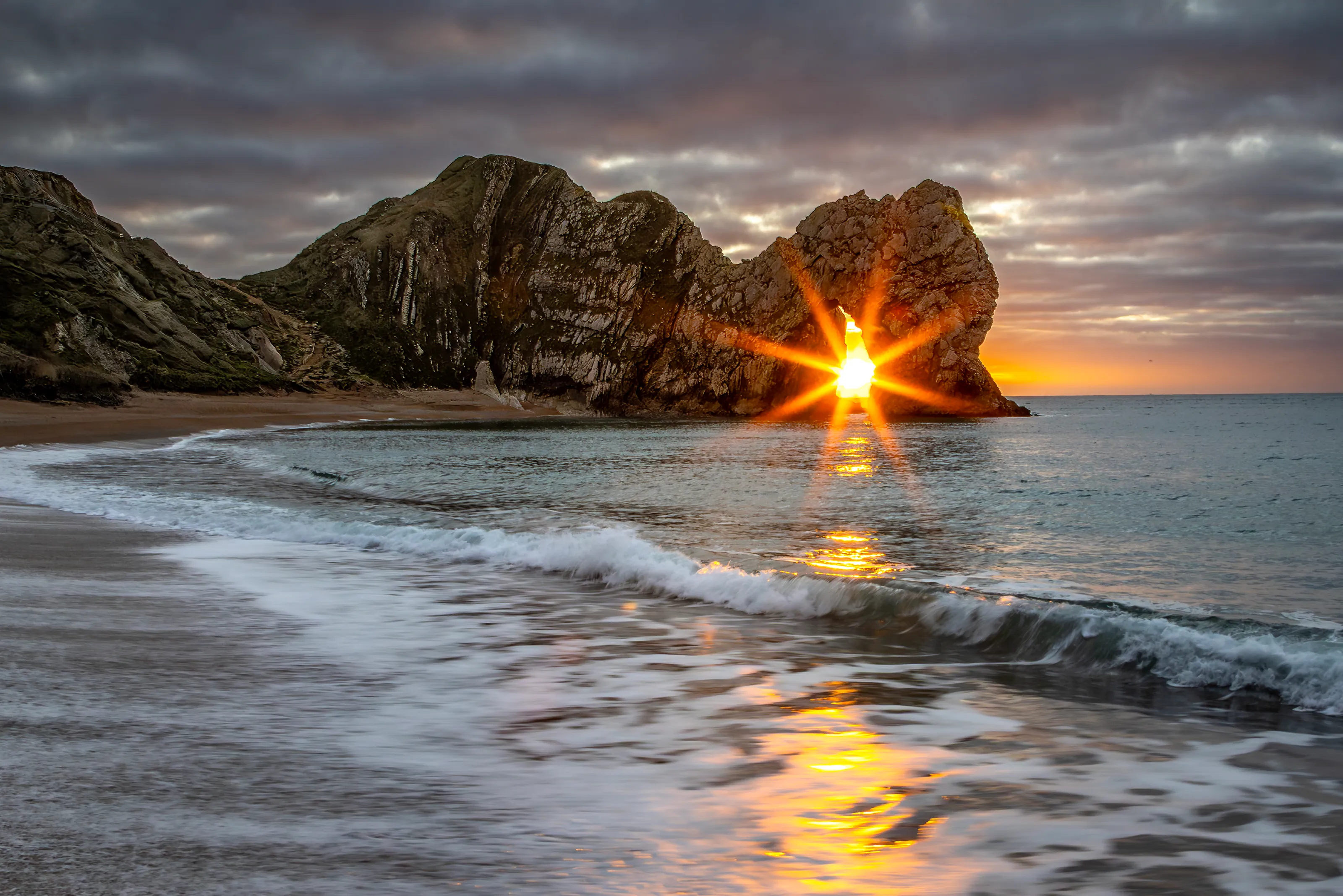 Sunstar, Sun seen rising through Durdle Door, Dorset, UK