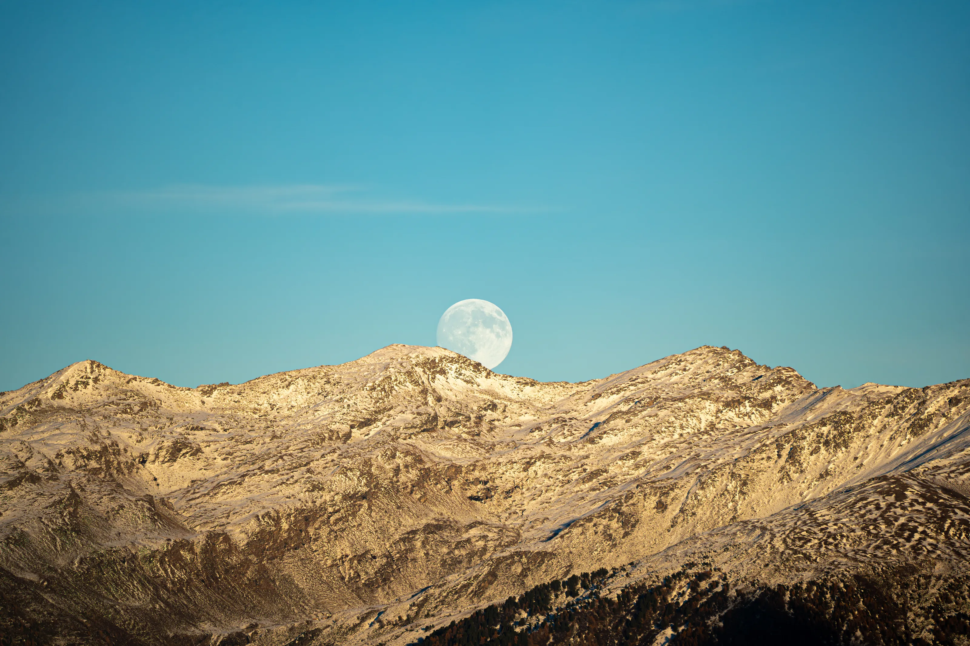 The supermoon in November 2025 captured at high altitude rising behind another mountain.