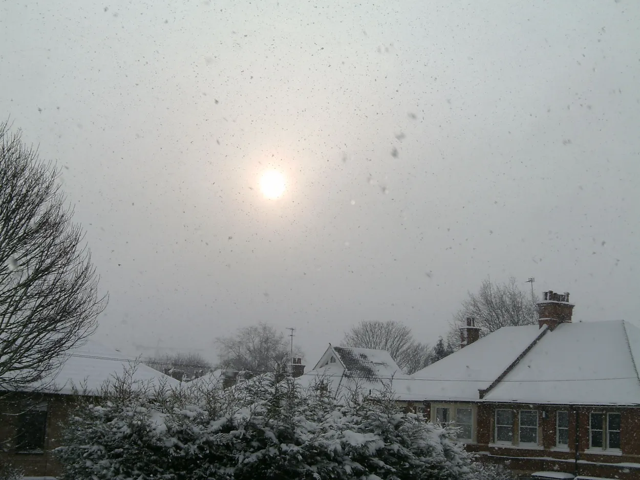 Muted sun shining above a snowy residential neighborhood during active snowfall