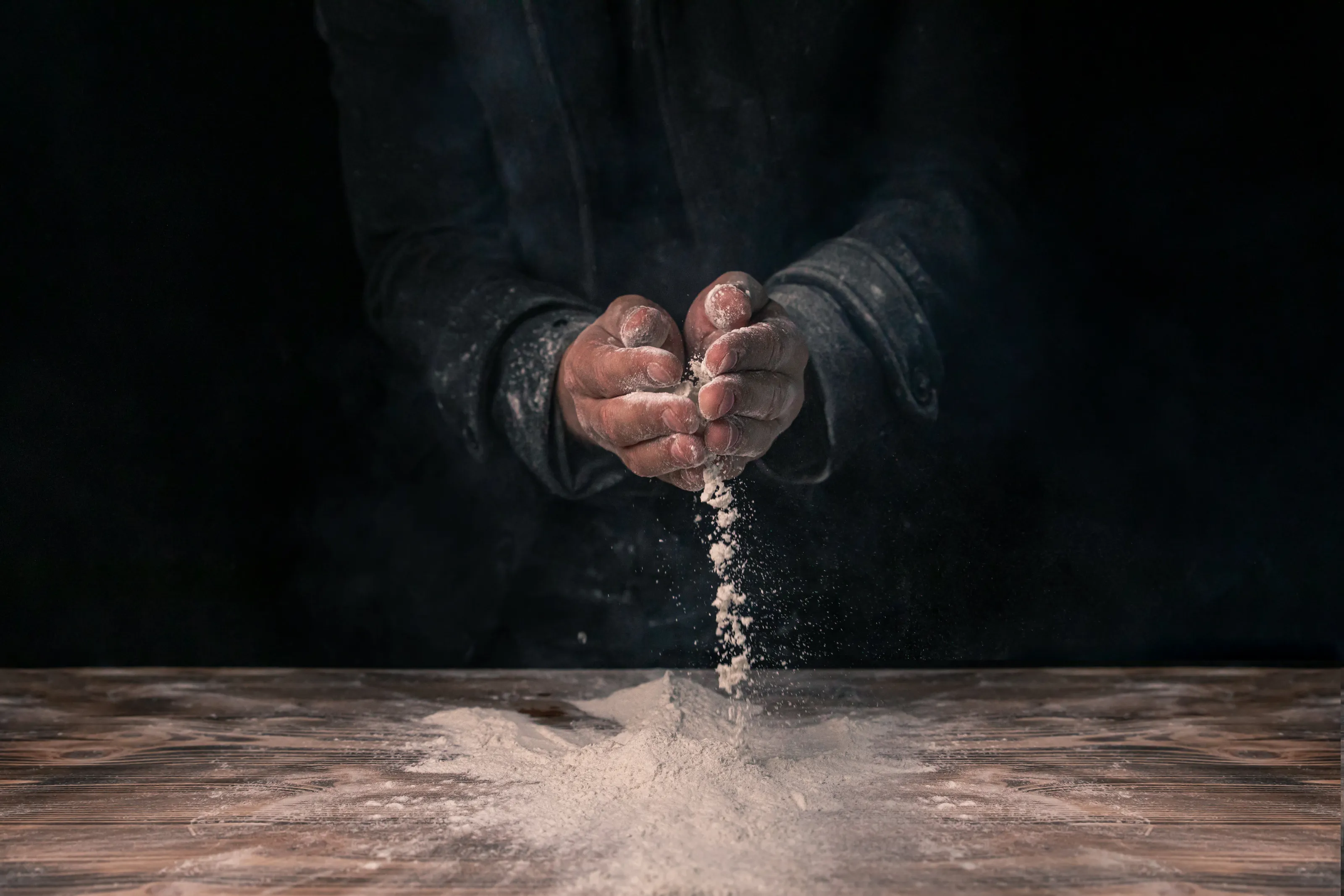 White flour flies from the hands in air on black background .