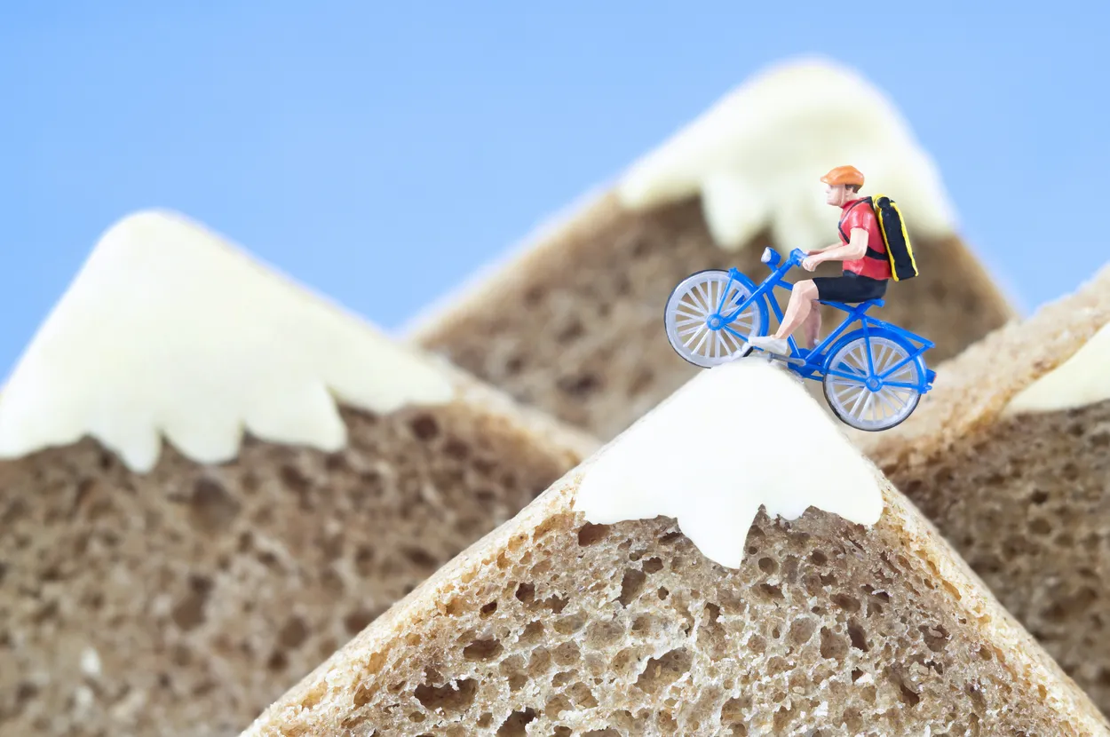 A toy cyclist is taking a ride on mountains, made of rye bread and creamy cheese.